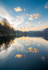 Calm water of Sirio Lake in Piedmont, dusk light, cloudy sky reflections