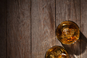 Glasses of whiskey with ice on wood