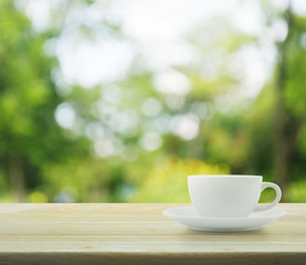 White cup on wooden table over tree bokeh background