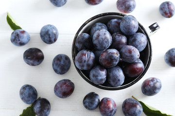 Fresh plums in cup on the white wooden background