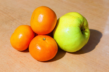 tangerines and an apple on a wooden table