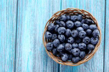 Tasty blueberries in basket on a blue wooden table