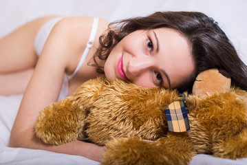 Joyful beautiful young woman in white underwear lying with teddy bear