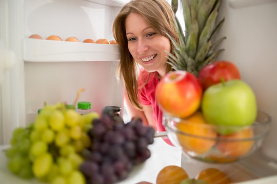 Smiling woman look fruit in refrigerator