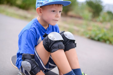 Thoughtful little boy sitting on a skateboard