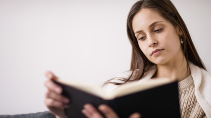 Young woman wearing a blanket and reading a book in comfort