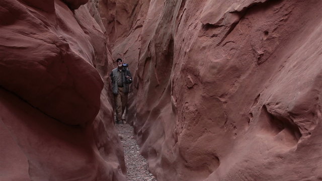 Photographer man hikes narrow desert slot canyon HD. Mature man takes video and photographs of southern Utah sandstone mountain valley. Dangerous area for flash floods. 1569