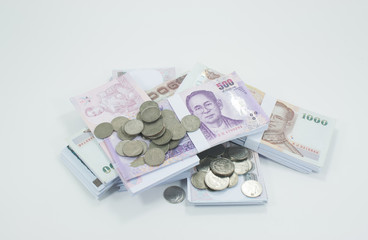 Old coins lay on a pile of banknotes on a white background.