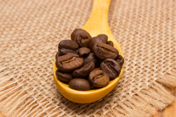 Heap of coffee beans with wooden spoon on jute canvas