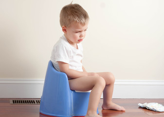 sad toddler boy wearing a white t-shirt sitting on a potty
