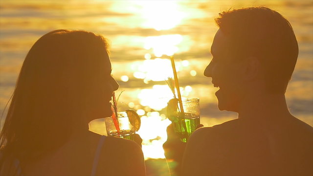 5 in 1 video! The lovers couple (pair) sit on the beach with cocktail by the bright sunlight reflection on the water surface background.
