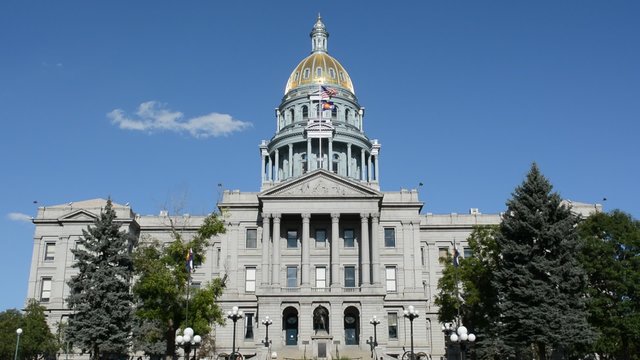 The Colorado State Capitol Building with a billowing American and Colorado flag on a sunny summer day.