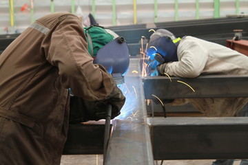 two welder are welding steel structure with all safety equipment  in factory