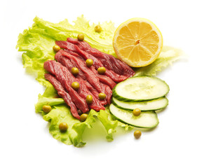 Raw meat decorated with lemon, cucumber, and salad over white background