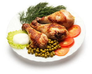 Chicken legs decorated with dill, pea and tomato over white background
