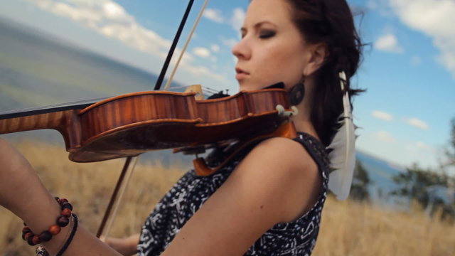 Young woman on the mountain playing the violin on sea background. Steadicam Shot
