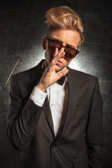 modern man in tuxedo posing while touching nose