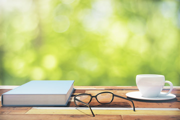 Book, cup of coffee and eyeglasses on a vintage wooden table in