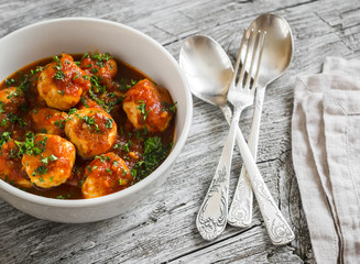 chicken meatballs with tomato sauce in a white bowl on bright wooden surface. Healthy food
