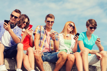 group of smiling friends with smartphones outdoors