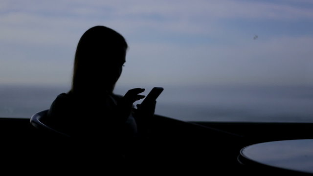 silhouette of young girl sits in a cafe with panoramic  window