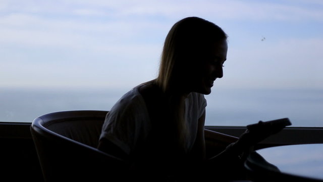 silhouette of young beautiful girl useing gadget and sitting in
