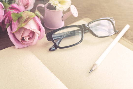 Open blank notebook with flower and glasses on wooden table
