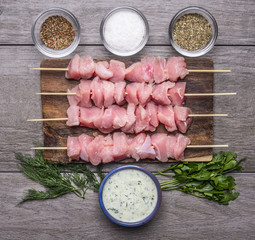 fresh raw chicken pieces on skewers Seasoned Salt and garlic sauce and greens on a cutting board