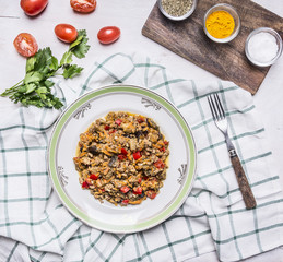 Georgian dish of lamb with eggplant and vegetables On a white plate with herbs and tomatoes and parsley with a fork on a checkered napkin on rustic wooden background top view