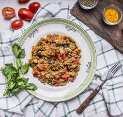 Appetizing lamb with vegetables on a white plate with tomato and parsley seasoned and fork on a checkered napkin top view close up