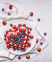 Fresh delicious homemade cake with strawberries and blueberries  In the form of heart In pink and white napkins on rustic wooden background close up top view