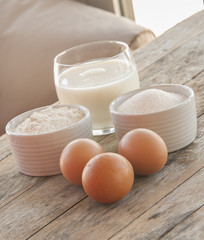 Ingredients for pancakes - eggs, flour, milk on wooden background.