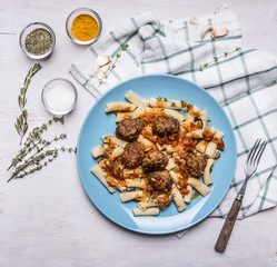 penne with  meatballs Sicilian by on a blue plate with a fork and spices on a checkered napkin on rustic wooden background close up top view