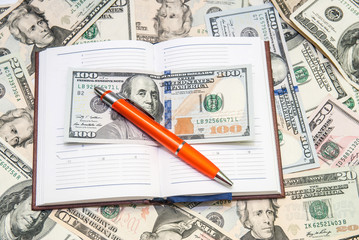 pen lying  on open notebook with dollars background