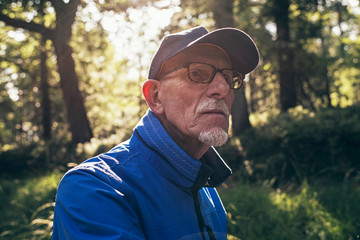 Retired active man with cap in summer forest. Backlit.