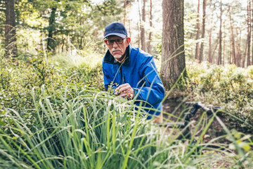 Retired active man standing with bicycle observing bushes.