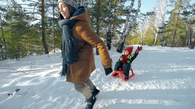 Slow motion shot of energetic boy pulling a sled with his laughing sister