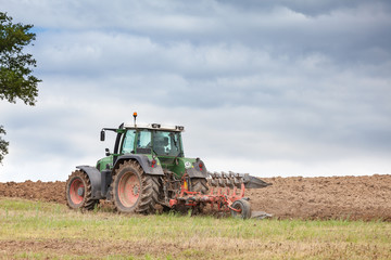 Farmer ploughing overwintered fields with a tractor and plough preparing the earth for the planting of the spring crop in an agricultural landscape
