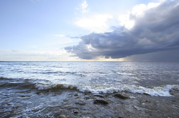 Fototapeta premium Storm cloud over the sea wave in front of stones.