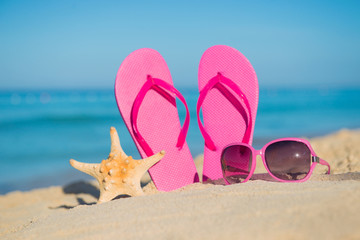 Fototapeta na wymiar The sea, beach, sand and women's accessories: pink flip-flops, sunglasses and starfish