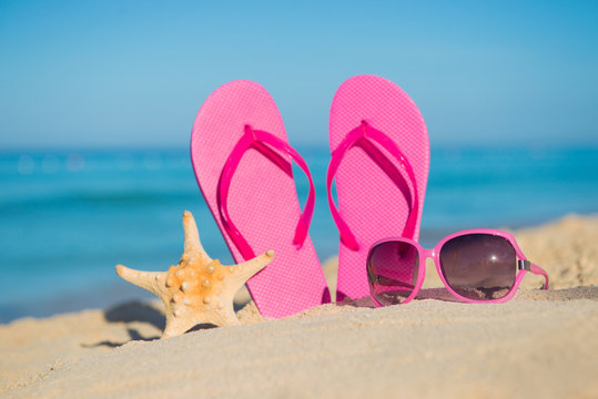 The sea, beach, sand and women's accessories: pink flip-flops, sunglasses and starfish