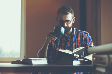 bearded man reading books and drinking coffee or tea