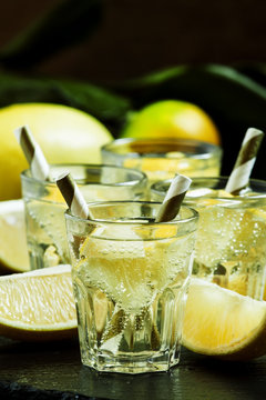 Carbonated lemonade with lemon slices on dark stone background,