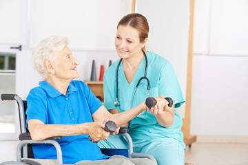 Fototapeta premium Seniorin im Rollstuhl hebt Hanteln bei Physiotherapie