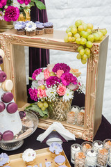 Decoration with pink, white and red flowers in golden wooden frame. Wedding decor with grapes and cookies