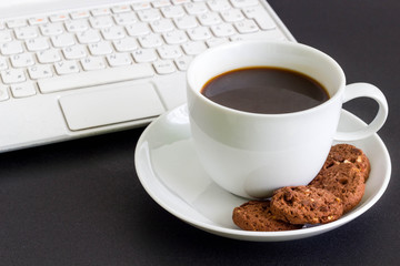 A cup of coffee with cookies, next to a laptop on a desk.