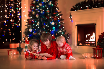 Fototapeta na wymiar Kids reading a book on Christmas eve at fireplace