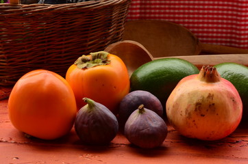 Figs, persimmons, pomegranate and avocados on rough background