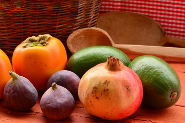 Figs, persimmons, pomegranate and avocados on rough background