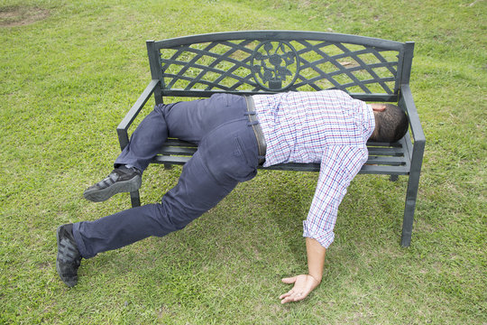 Hombre afroamericano ebrio dormido en banca de parque. 